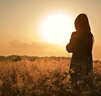 אישה עומדת בשדה מול השמש בשקיעה